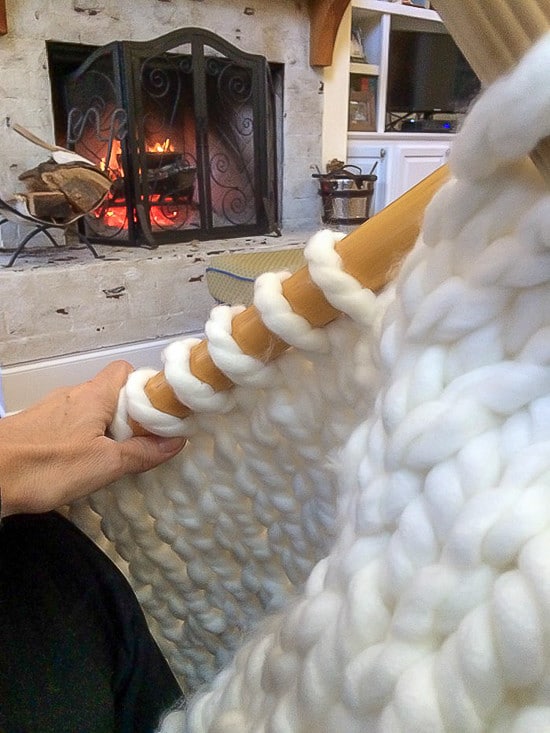 knitting a chunky knit blanket in front of the fireplace